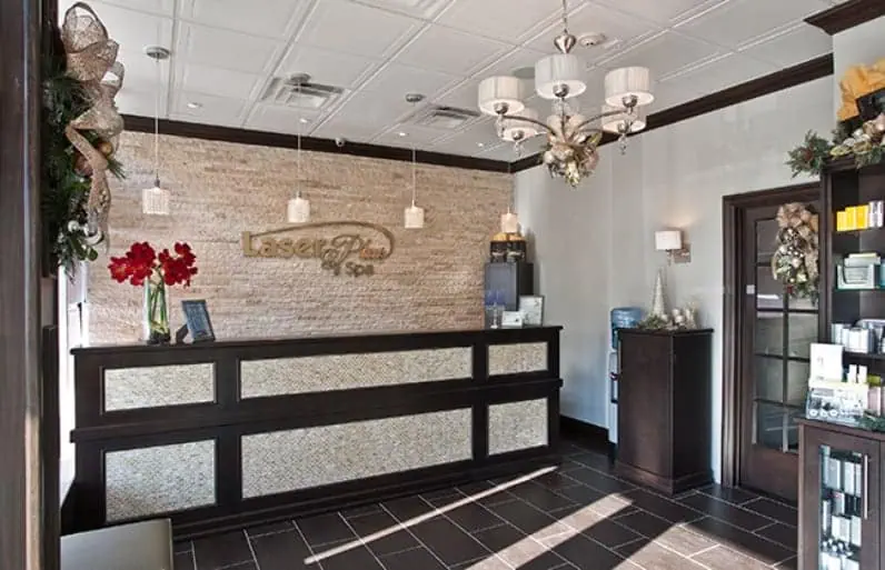 The reception area of the spa, crafted by top interior designers in Long Island, NY, features a stone accent wall, a chandelier, and a wooden desk. Red flowers and wreaths add charm, while shelves of skincare products on the right enhance the cozy and welcoming atmosphere.