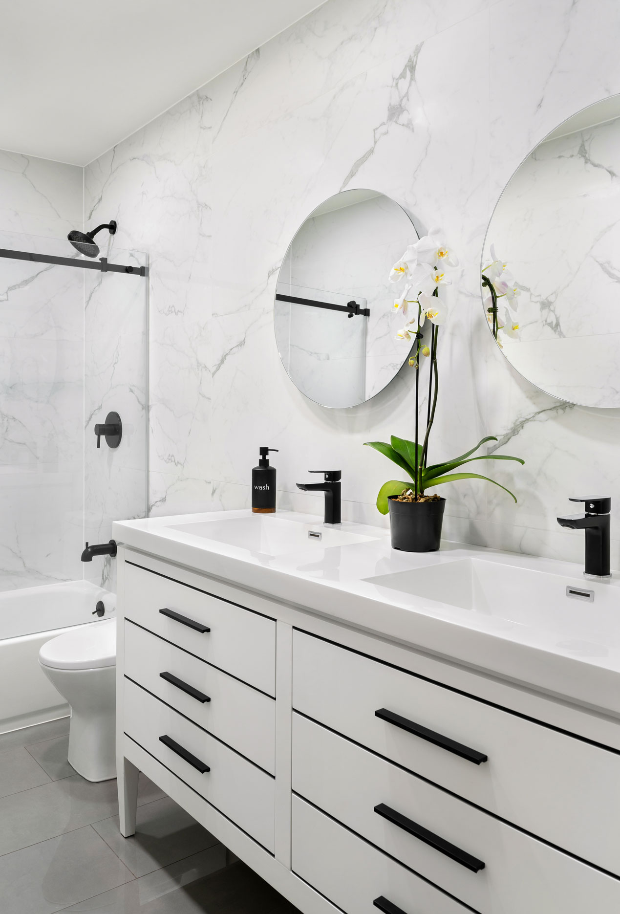 White marble walls in bathroom with white vanity and dark fixtures