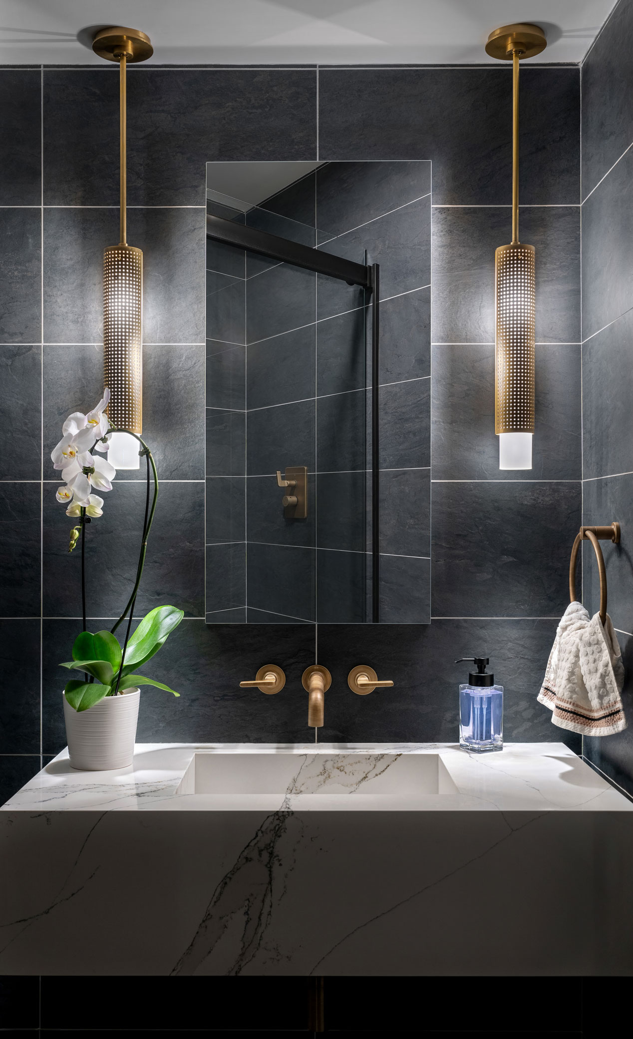 large dark gray tiles on bathroom walls with bronze fixtures and marble sink