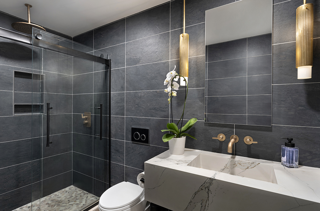 bathroom with extra large dark gray tiled walls with brass fixtures
