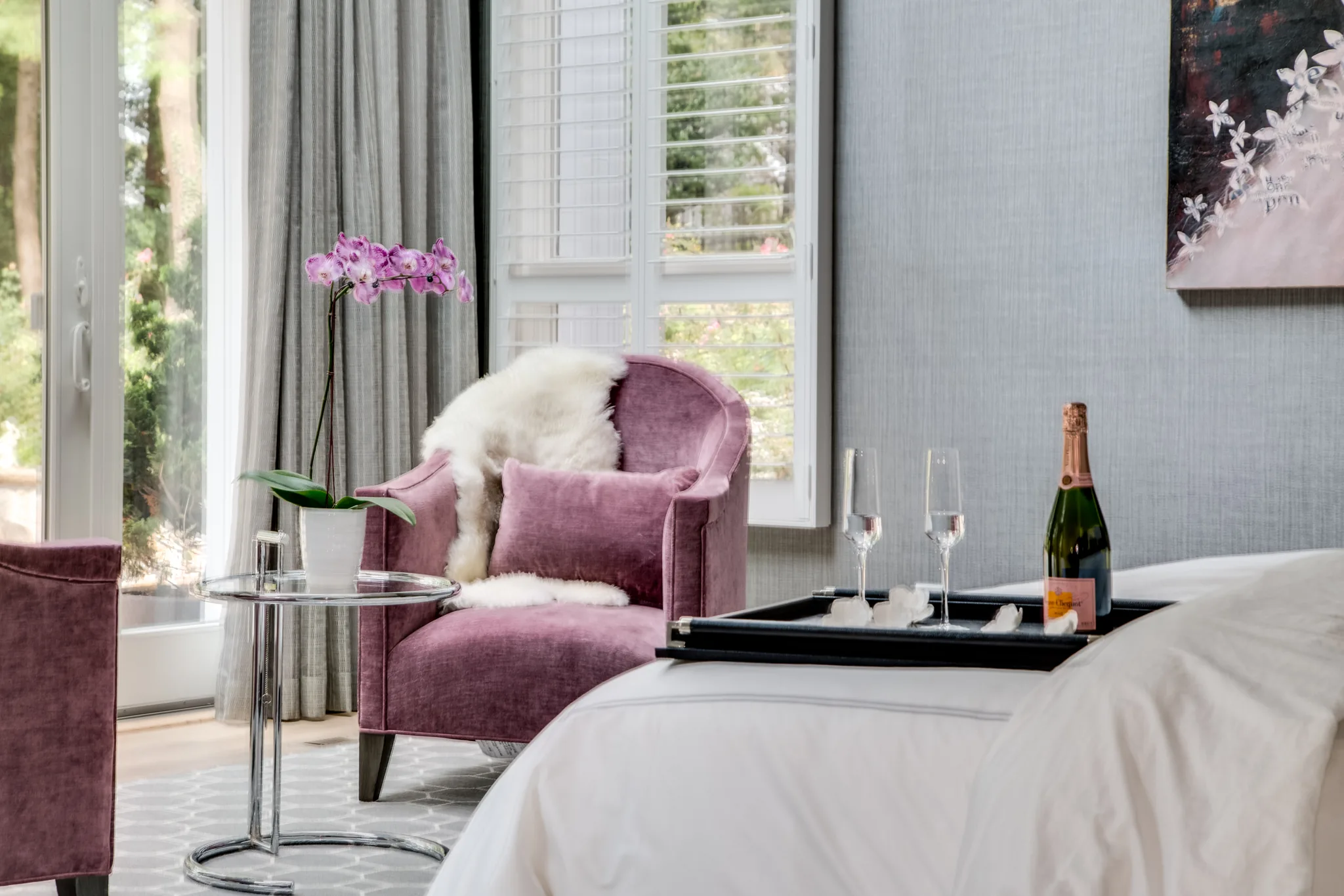 white bedding with purple arm chairs near large windows