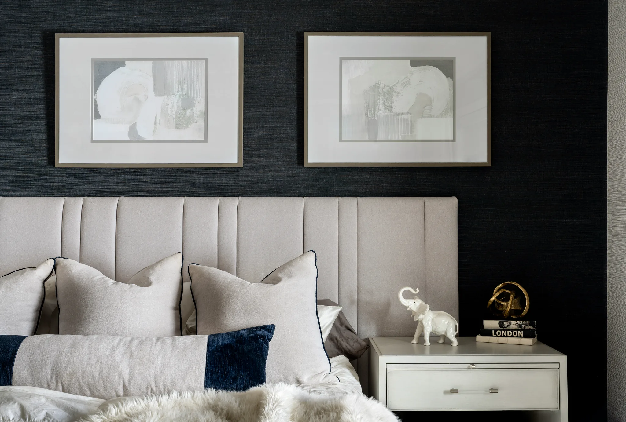 bedroom with black walls and plush white headboard. bed is white linens with white pillows and black accents