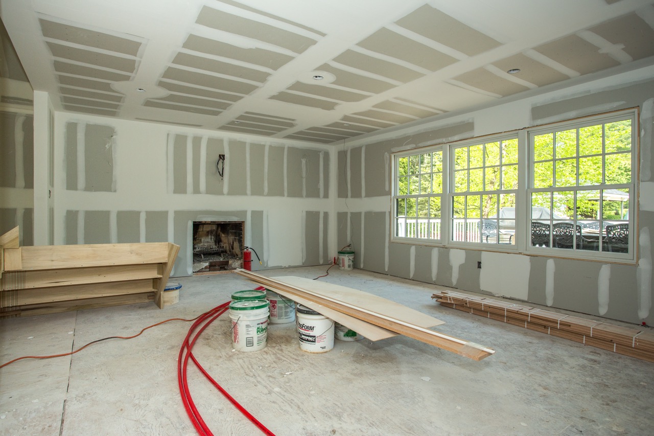 Family room under construction with drywall, a brick fireplace opening, and stacked hardwood flooring by the windows