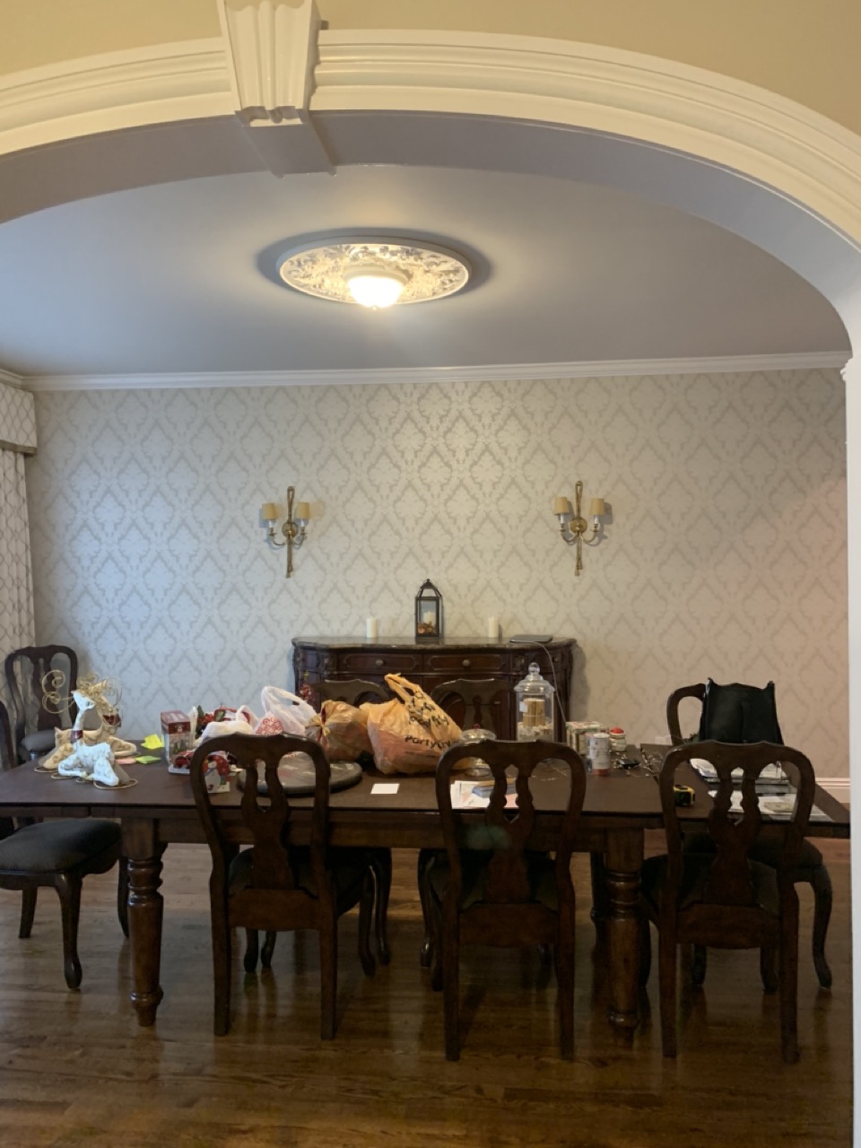 Dining room before renovation with light damask wallpaper, brass sconces, a dark traditional table, and an arched entry