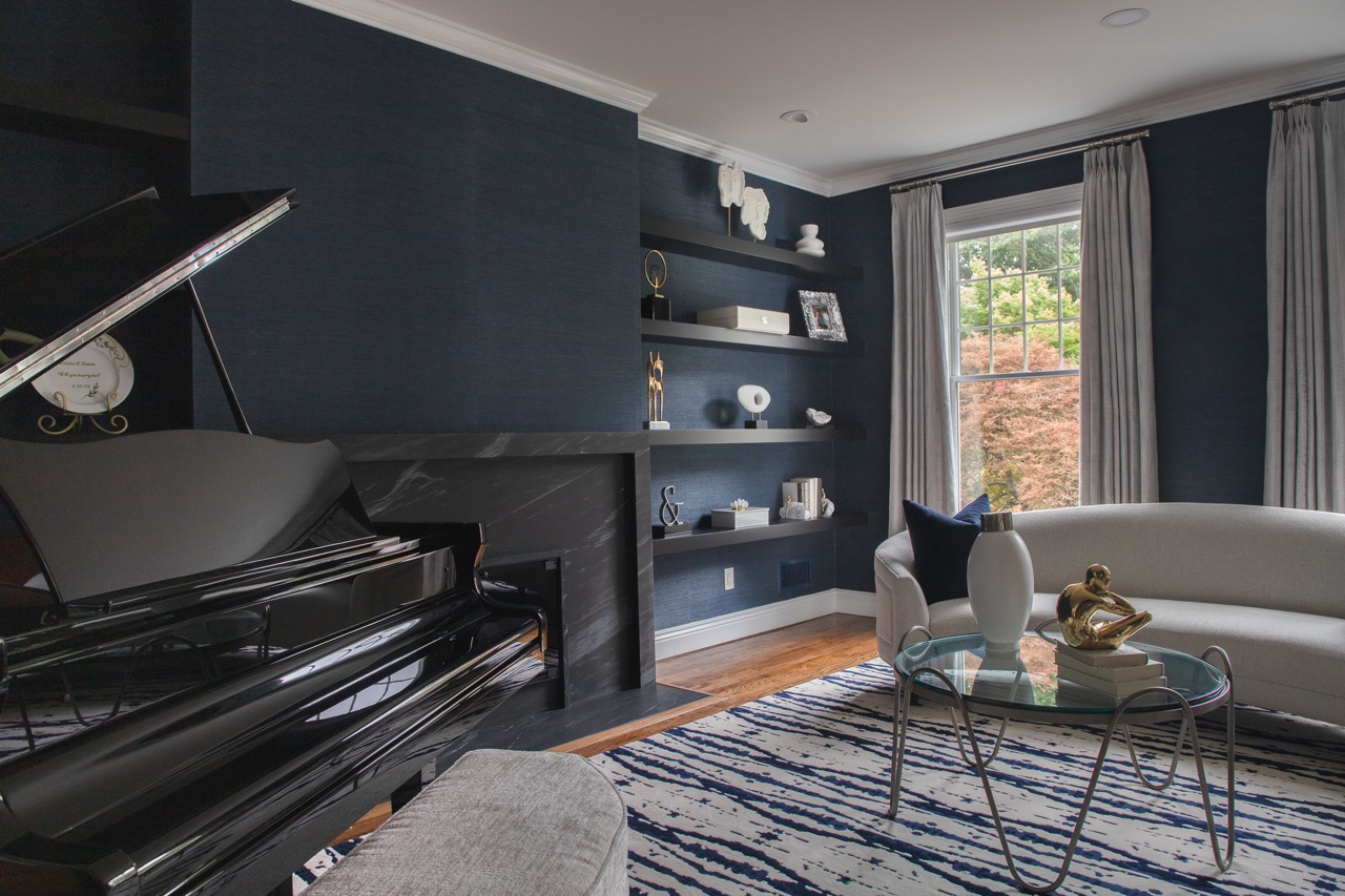 Navy living room detail showing floating shelves styled with sculpture, a marble mantel, and the open baby grand piano