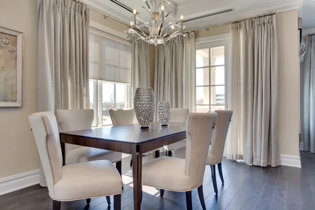 dining room with dark wood flooring, beige walls and curtains, and dark dining table with plush chairs