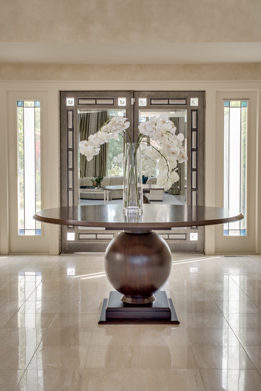 classic entranceway in the Hamptons - large rounded table with floral decor in from of a large double front door
