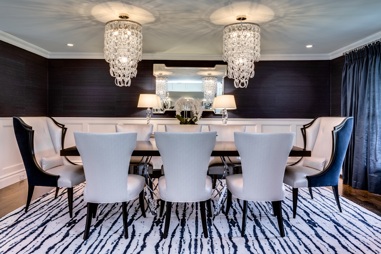 Formal dining room with dark grasscloth walls, white wainscoting, twin crystal chandeliers, and a black-and-white zebra-pattern rug