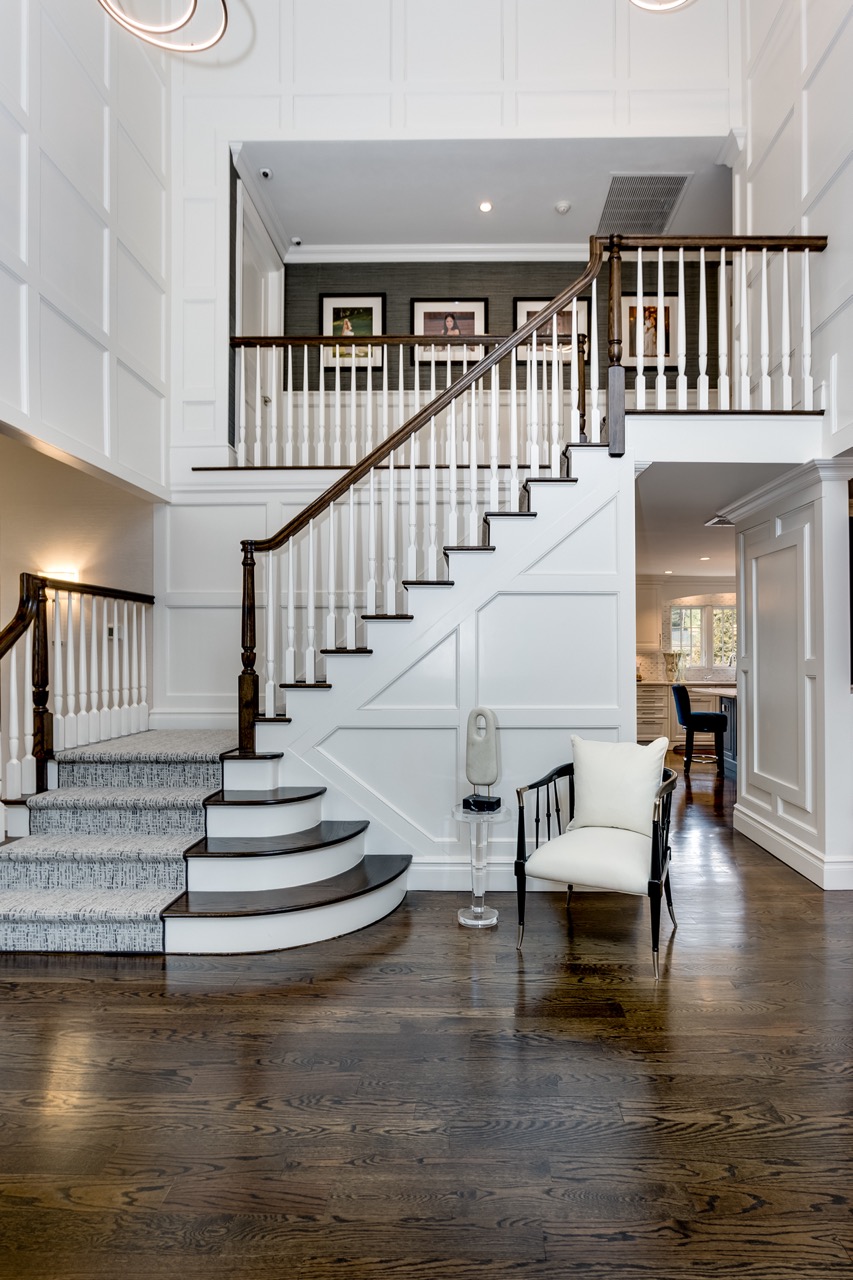 Finished two-story foyer with curved dark-stained staircase, white paneled walls, patterned runner, and accent chair