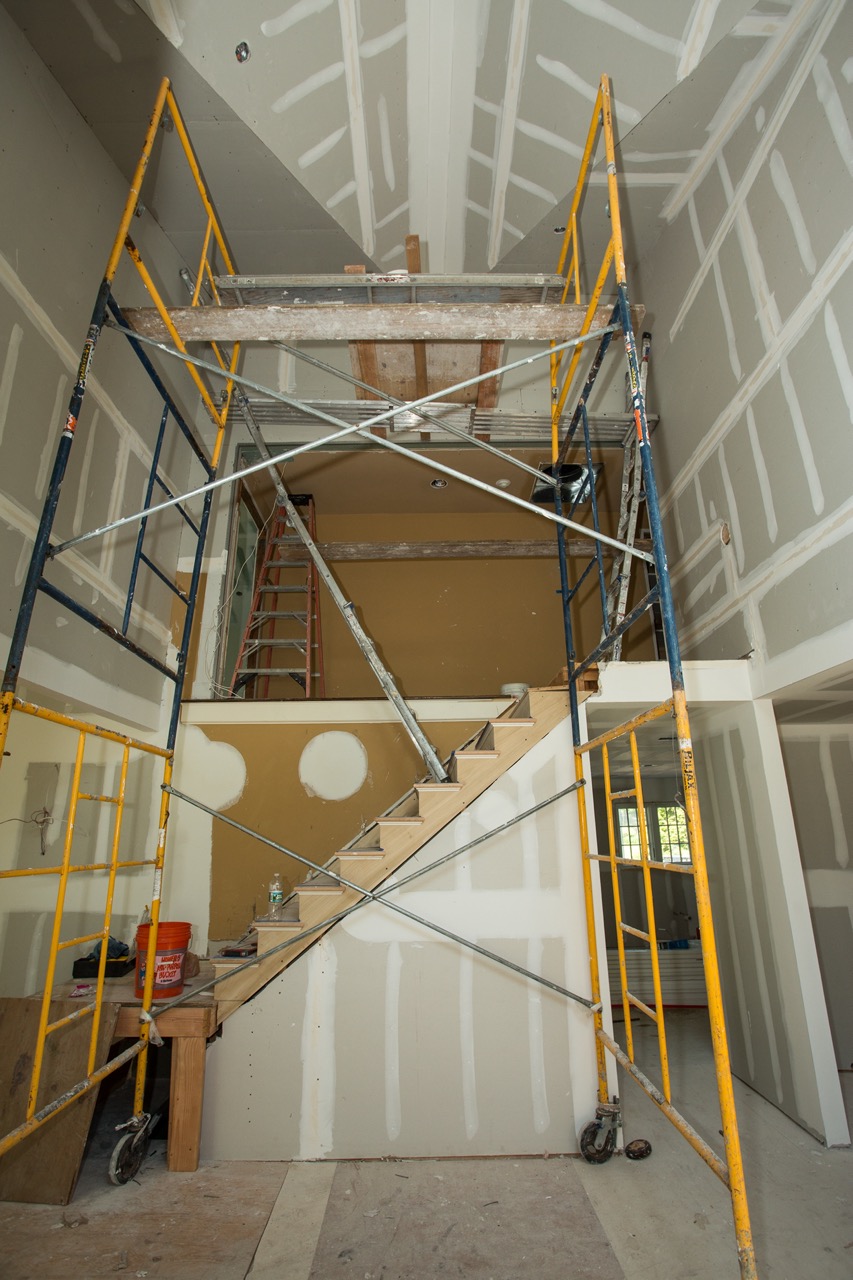 Two-story foyer during construction with scaffolding around the framed staircase and unfinished drywall