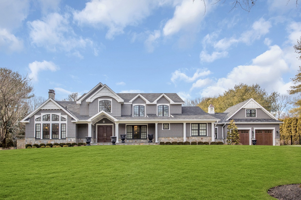 Stone and grey shingle new-construction home in Old Westbury with gabled roofline, covered porch, and attached garage