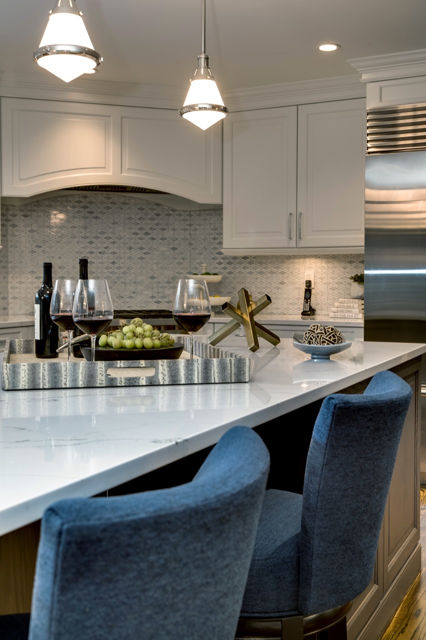 Kitchen island close-up with marble waterfall counter, blue swivel stools, schoolhouse pendants, and patterned tile backsplash