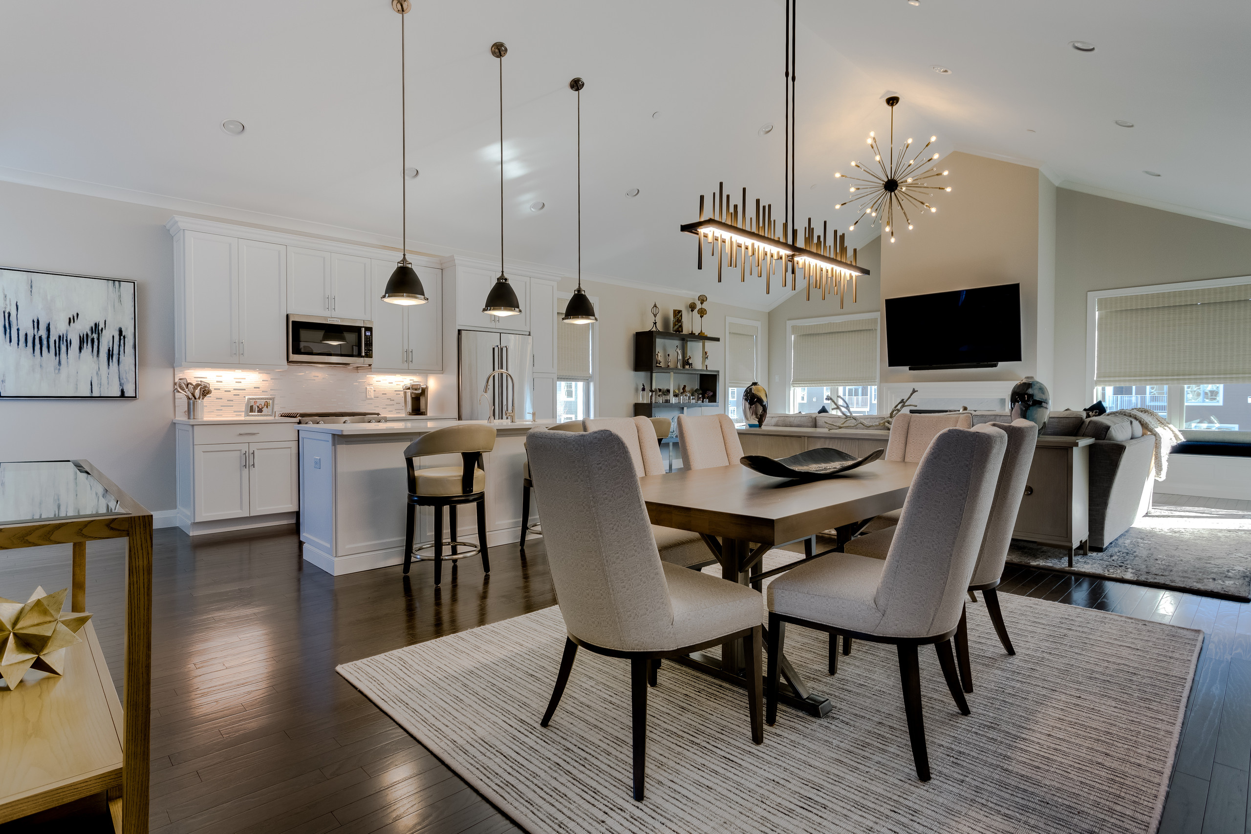 Dining room with warm wood table, cream upholstered chairs, and a linear brass and black chandelier under a vaulted ceiling