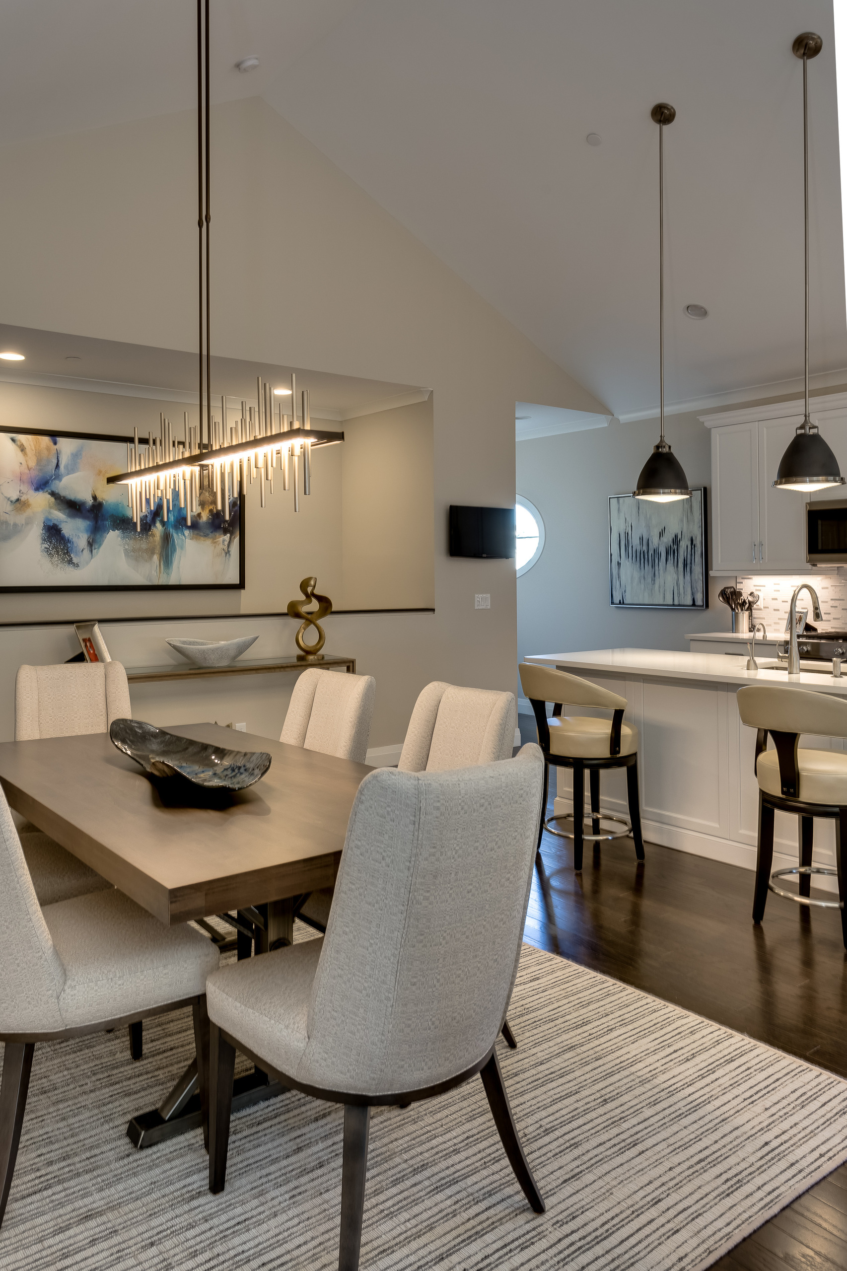 View from the dining table toward the white kitchen, with black pendant lights and cream leather counter stools
