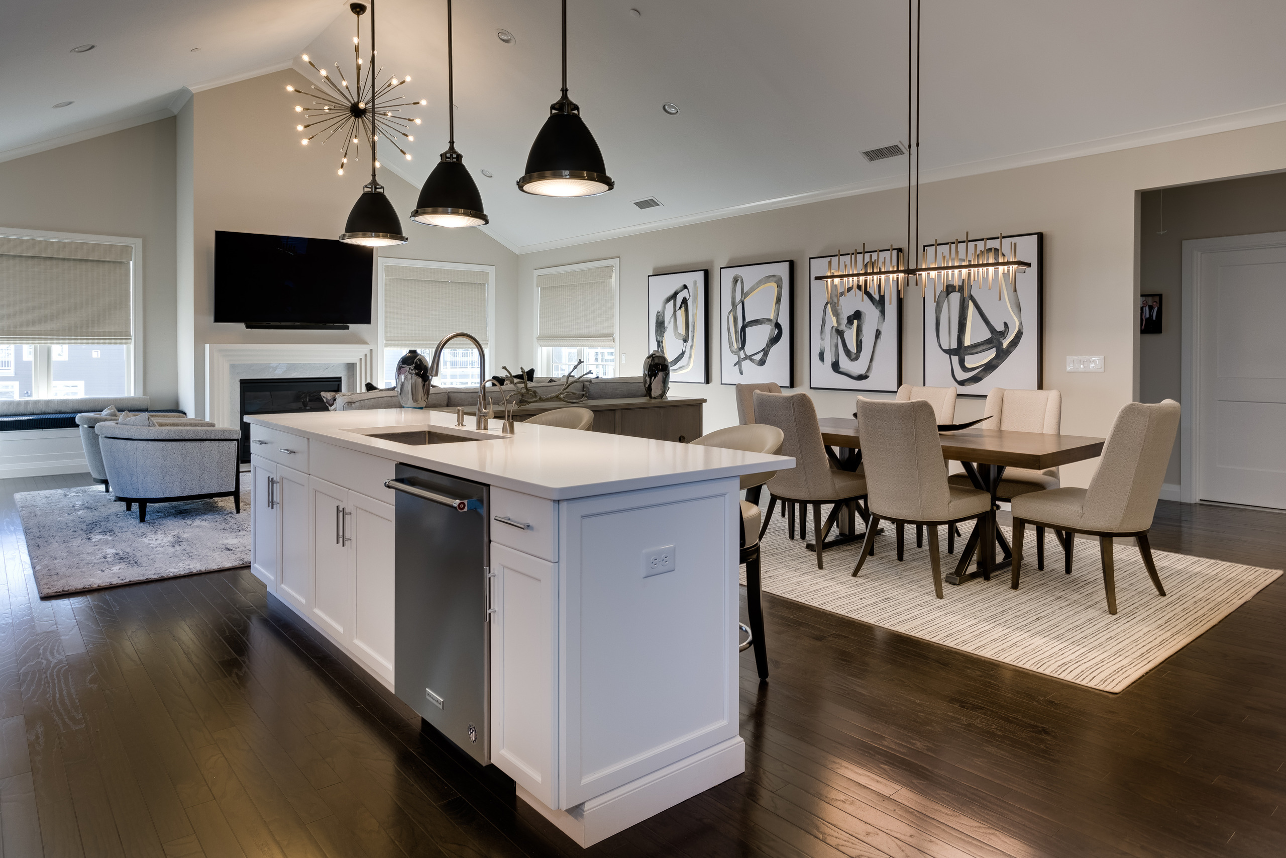 Open plan condo with white kitchen island, black pendant lights, dining table, and living area with fireplace