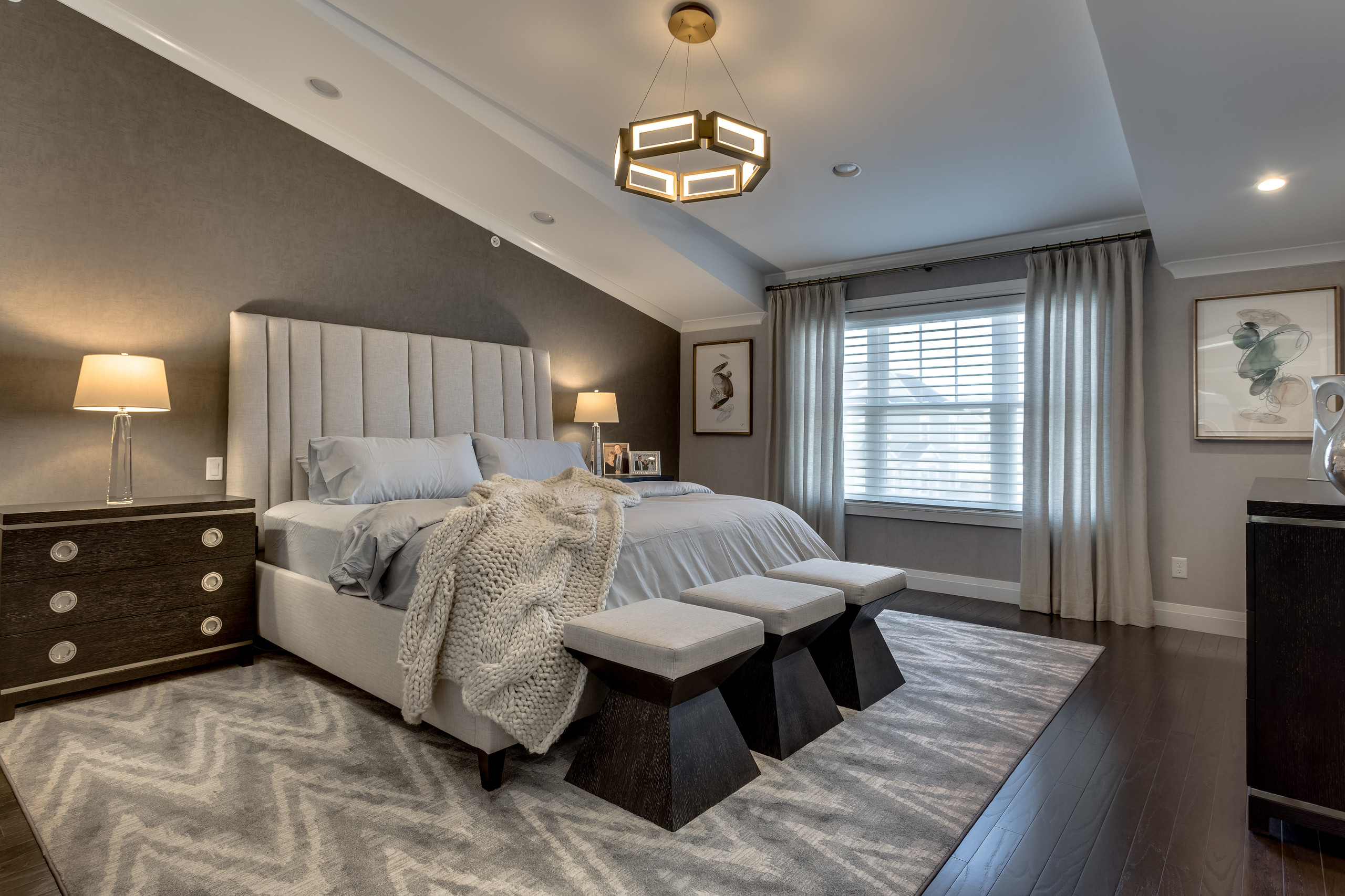 Primary bedroom with tall channel-tufted cream headboard, taupe grasscloth wall, and three angled-base benches at the foot of the bed