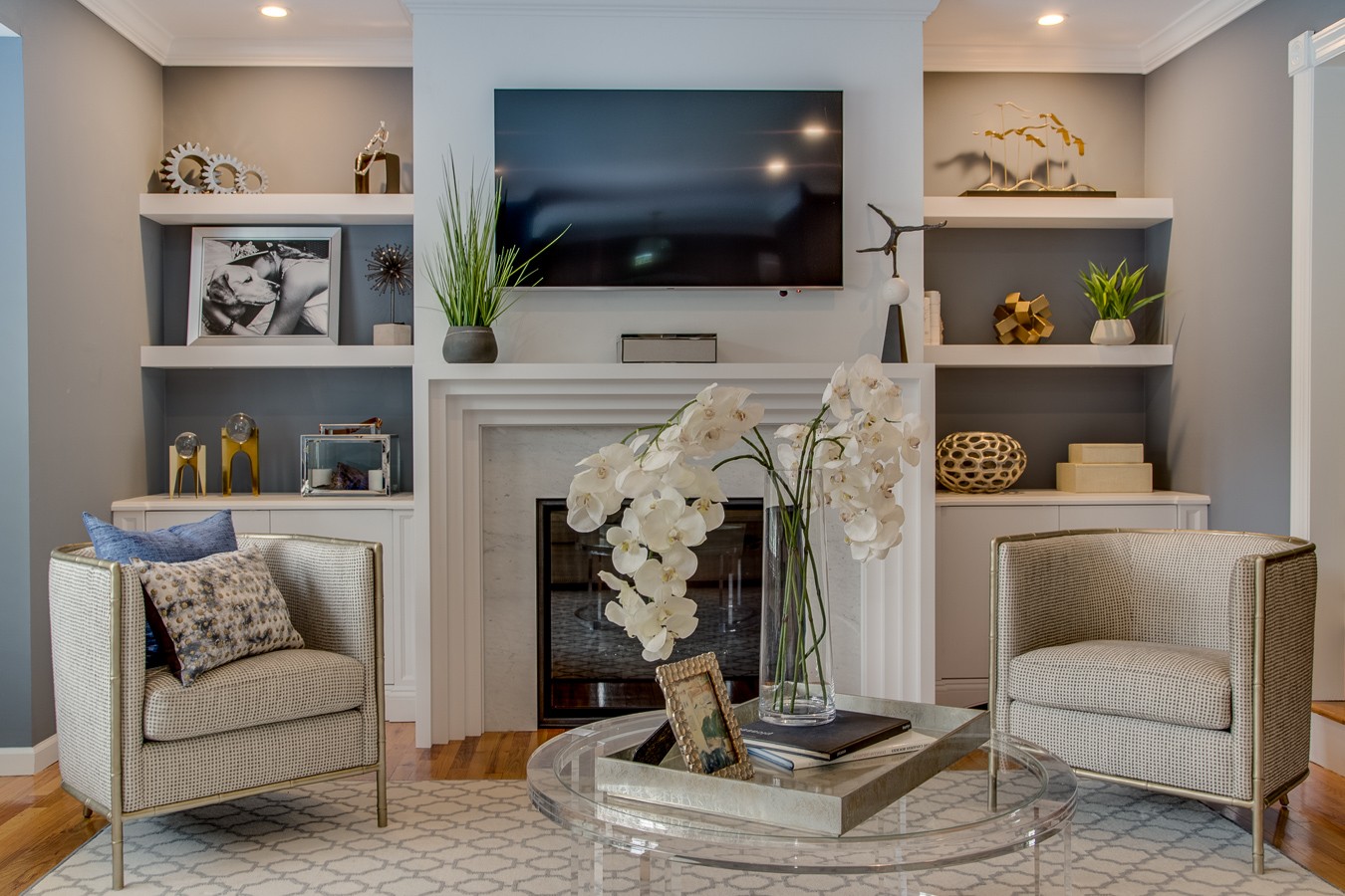 Living room fireplace wall with deep blue built-ins, white stepped mantel, mounted TV, and two woven barrel chairs