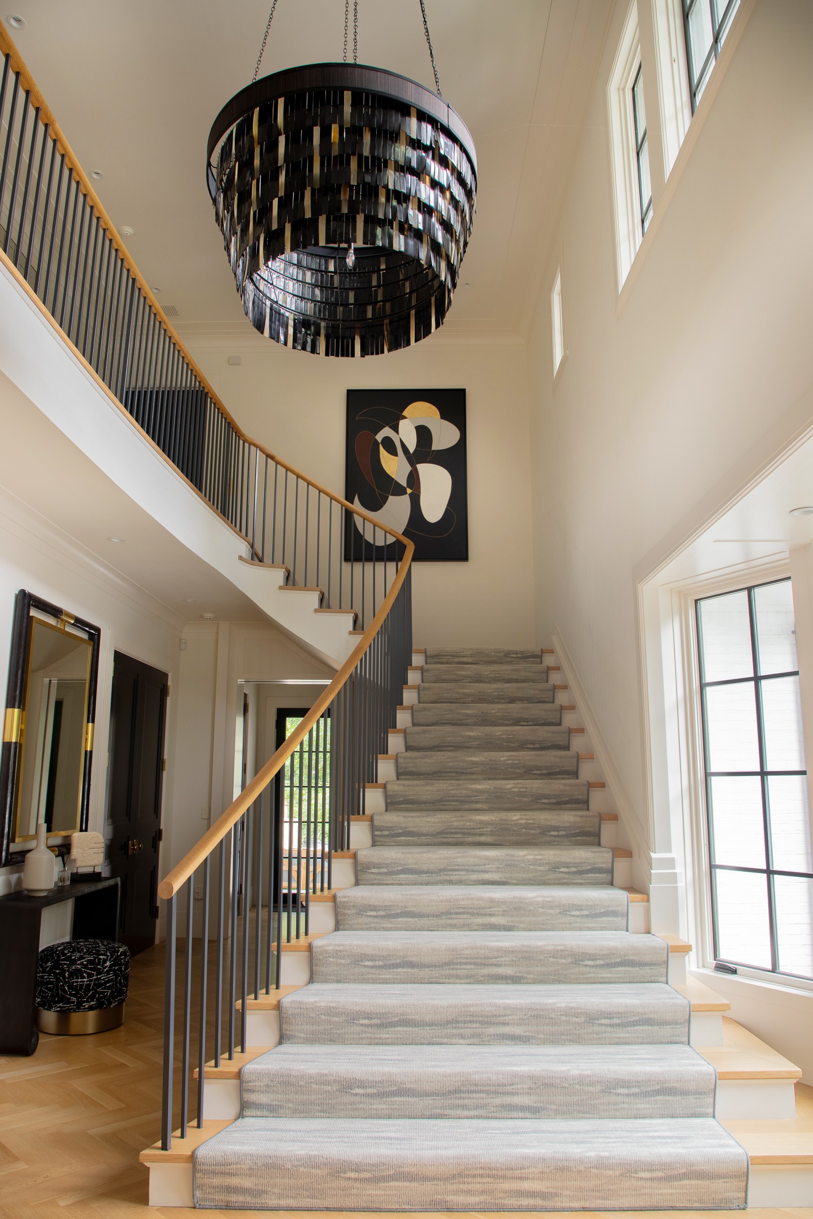 Two-story foyer with tiered black chandelier, curved staircase, and custom abstract artwork in black, white, and gold
